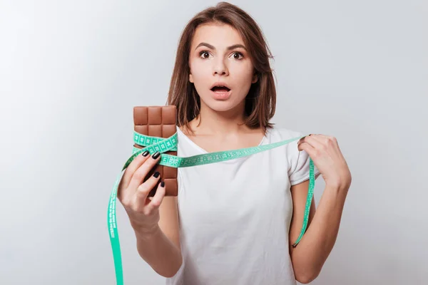 Förvirrad ung dam holding centimeter och choklad — Stockfoto