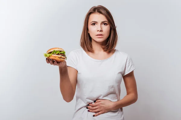 Verward jonge vrouw houdt van Fast-Food en aanraken van de buik — Stockfoto