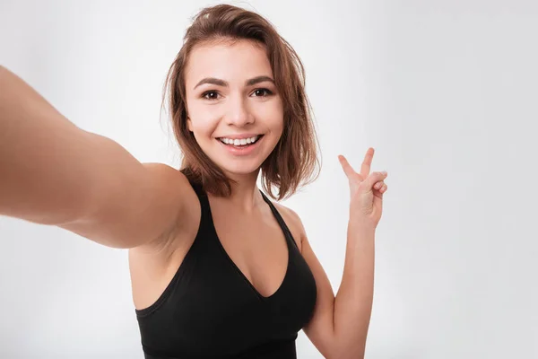 Happy young fitness woman make a selfie with peace gesture — Stock Photo, Image