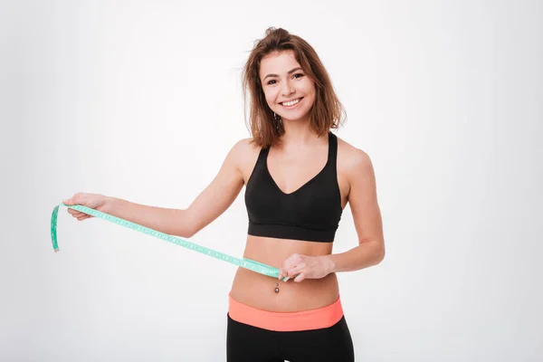 Cheeful aantrekkelijke jonge vrouw atleet permanent en het gebruik van meetlint — Stockfoto