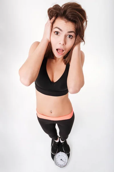 Surprised young woman athlete standing on weighting scale and shouting — Stock Photo, Image