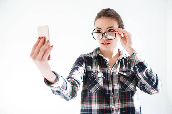 Жінка дивиться через окуляри і приймає селфі з мобільним телефоном — стокове фото