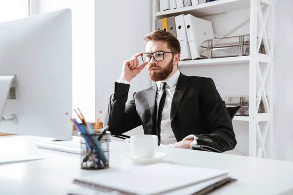 Concentrated young bearded businessman sitting in office — Stock Photo, Image