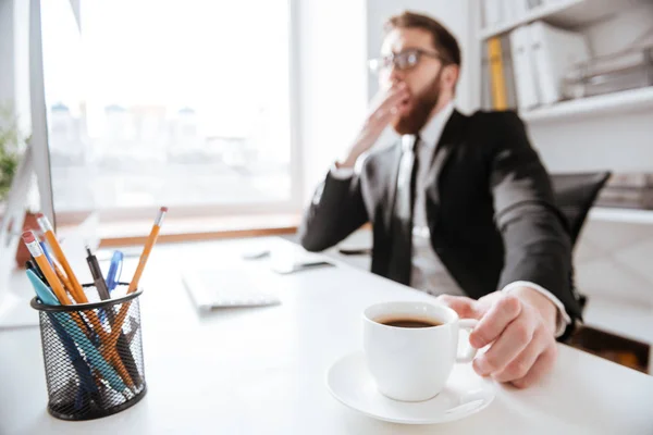 Bebaarde zakenman houden van koffie en geeuwen — Stockfoto