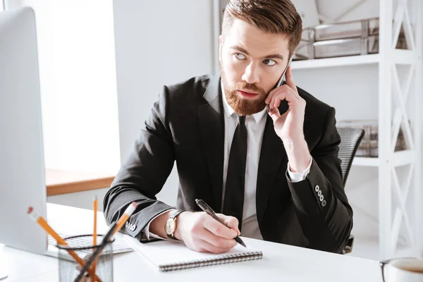 Hombre de negocios concentrado hablando por teléfono y escribiendo notas . — Foto de Stock