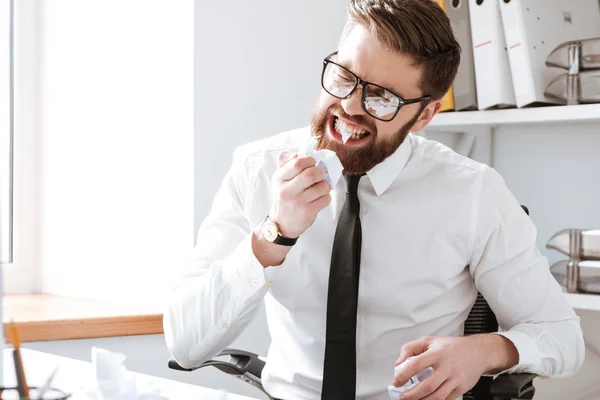 Enojado hombre de negocios sentado en la oficina y lágrimas de papel con dientes — Foto de Stock