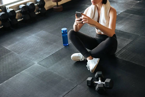 Sportowiec kobieta siedzi i przy użyciu telefonu komórkowego w siłowni — Zdjęcie stockowe