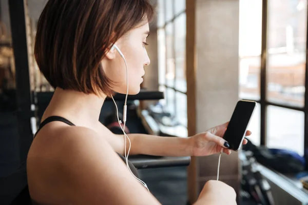 Fitness woman with earphones listening to music from mobile phone — Stock Photo, Image