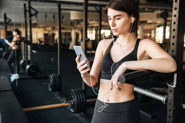 Sportswoman listening to music with cell phone in gym — Stock Photo, Image