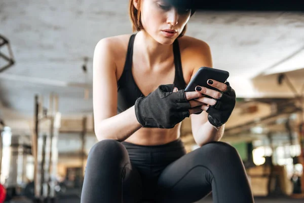 Mujer atleta sentada y usando smartphone en gimnasio — Foto de Stock