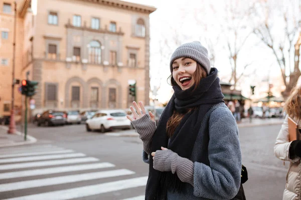 Feliz joven mujer de pie y mostrando un gesto de saludo en la ciudad — Foto de Stock