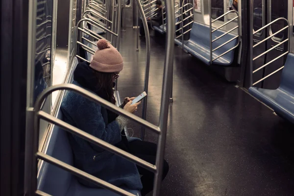 Jovem mulher usando telefone celular enquanto sentada no trem do metrô — Fotografia de Stock