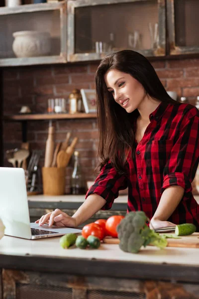 Вертикальное изображение женщины, стоящей на кухне с ноутбуком — стоковое фото