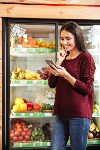Glückliche junge Frau mit Handy im Lebensmittelladen — Stockfoto