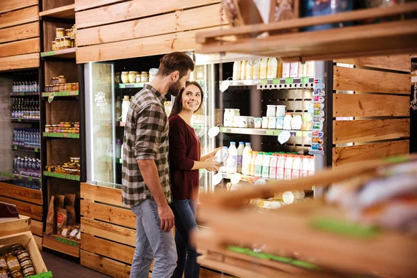 Lächelndes Paar steht im Supermarkt und wählt Milch — Stockfoto