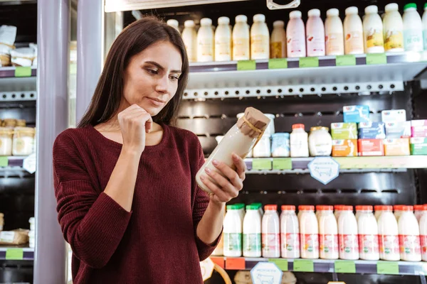 Töprengő fiatal nő kiválasztása joghurt élelmiszerüzlet — Stock Fotó