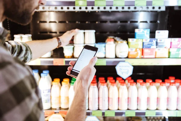 Hombre usando el teléfono móvil en las compras en la tienda de comestibles —  Fotos de Stock