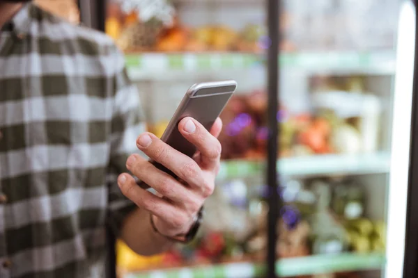 Teléfono celular utilizado por el hombre en la tienda de comestibles — Foto de Stock