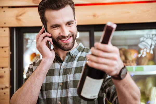 Happy young man buying wine and talking on cell phone