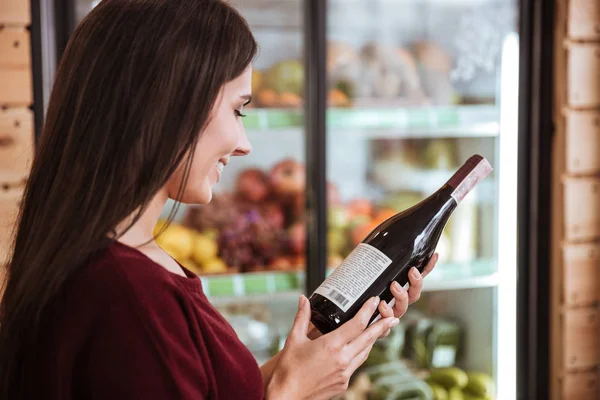 Женщина стоит и выбирает вино в продуктовом магазине — стоковое фото