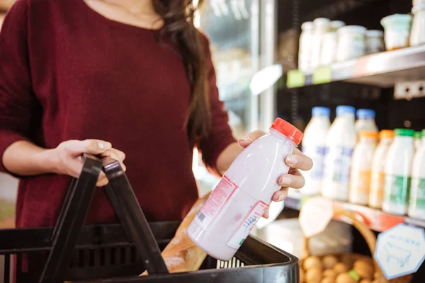 Жінка з кошиком купує молочний продукт в продуктовому магазині — стокове фото