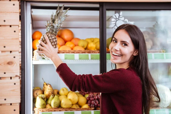 Femeia tânără veselă cumpără ananas în magazinul alimentar — Fotografie, imagine de stoc