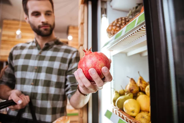 Мужчина выбирает и покупает гранат в продуктовом магазине — стоковое фото