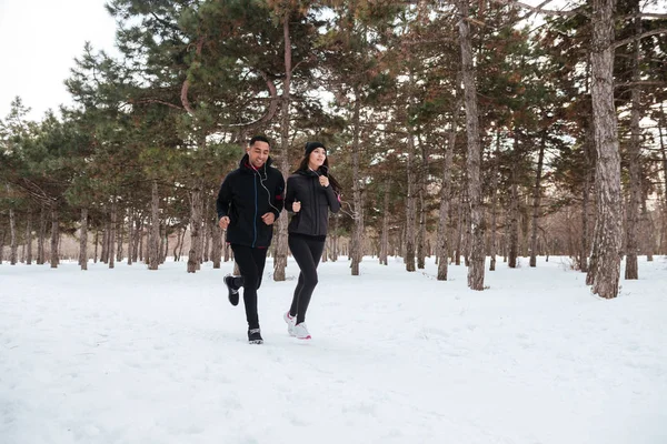 Jovem casal saudável correndo fora na neve na floresta — Fotografia de Stock