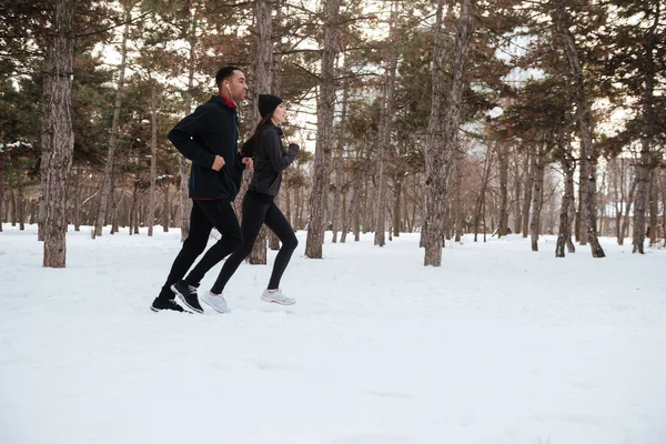 Pareja joven y saludable trotando afuera en la nieve en el bosque —  Fotos de Stock