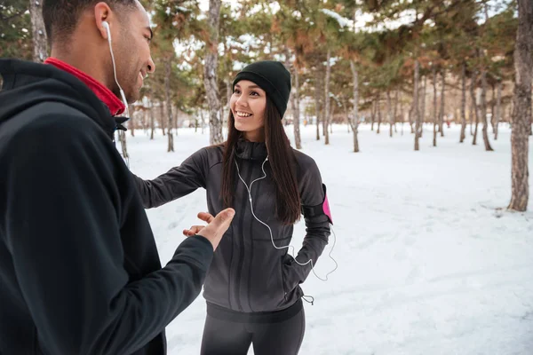 Casal conversando enquanto descansa depois de correr na floresta de inverno — Fotografia de Stock