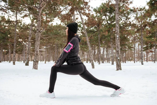 Fitness woman runner stretching legs before workout outdoors in winter — Stock Photo, Image