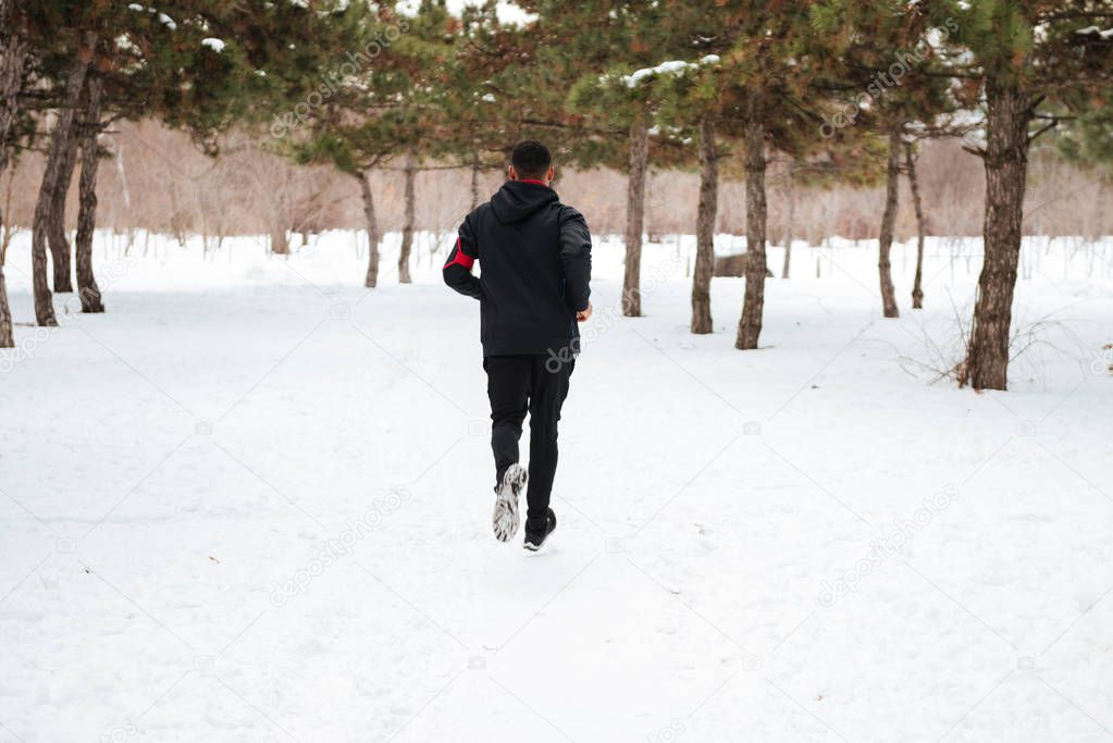 Young man running on snow covered winter road in forest