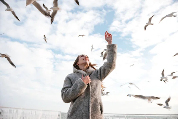 Mulher sorridente olhando para gaivotas no céu no inverno — Fotografia de Stock