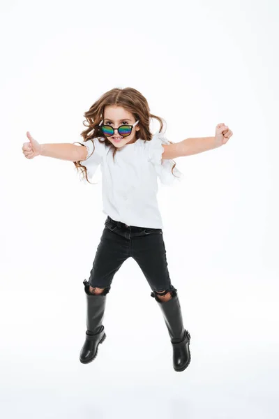 Smiling little girl in sunglasses jumping and showing thumbs up — Stock Photo, Image