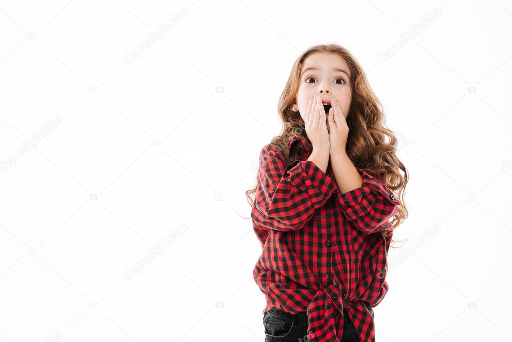 Surprised curly little girl covered opened mouth by hands
