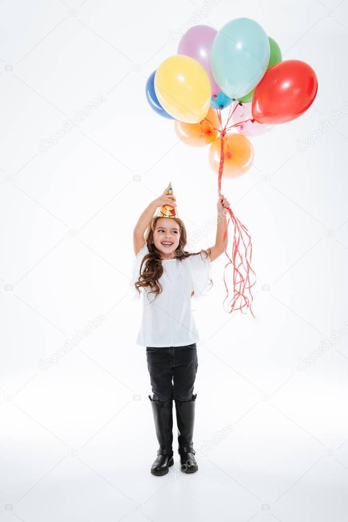 Cheerful girl in birthday hat with balloons standing and laughing