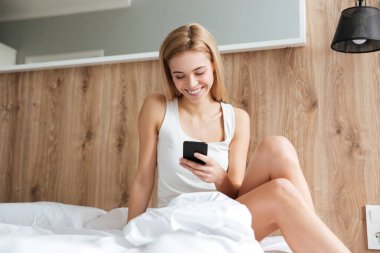 Gülümseyen kadın yatakta telefon kullanarak