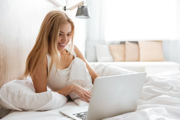 Donna sorridente utilizzando il computer portatile sul letto — Foto Stock