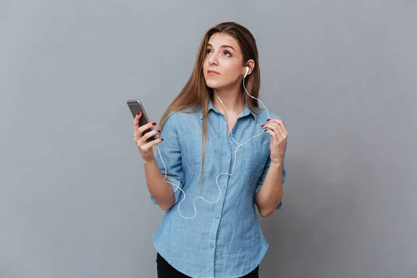 Eftertänksam kvinna i skjorta lyssnar musik på telefon — Stockfoto