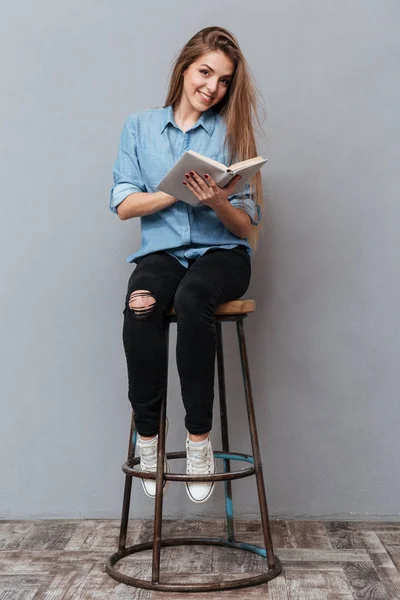 Függőleges kép nő ül a székre, és könyvet olvas — Stock Fotó
