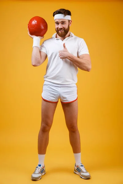 Cheerful young sportsman holding ball make thumbs up gesture — Stock Photo, Image