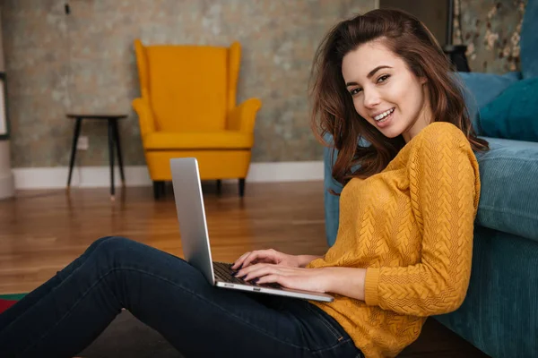 Mujer bonita sonriente sentada en el suelo apoyada en el sofá — Foto de Stock