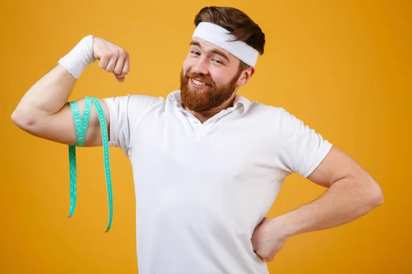 Retrato de un hombre musculoso sonriente midiendo bíceps con cinta métrica — Foto de Stock