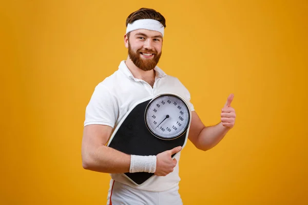 Fitness man holding weight scales and showing thumbs up — Stock Photo, Image