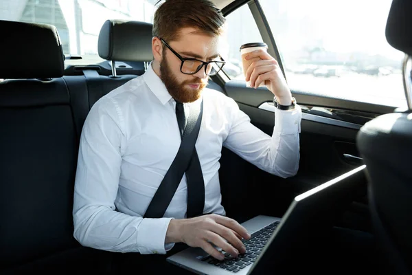 Hombre de negocios concentrado utilizando el ordenador portátil y la celebración de la taza de café — Foto de Stock