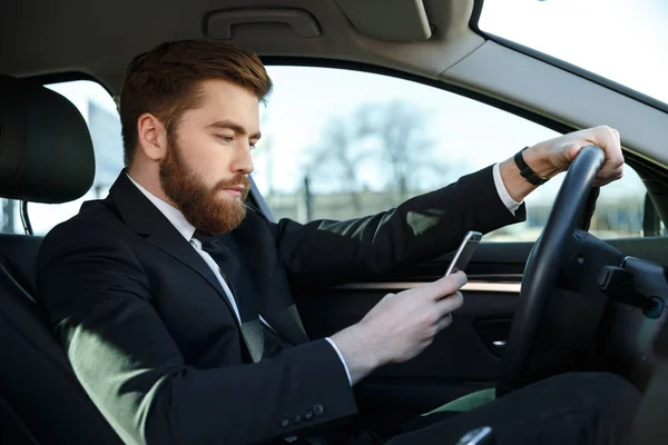 Side view of serious business man using phone at wheel — Stock Photo, Image