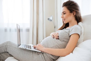 Hamile kadın yatakta yatak odasında dizüstü bilgisayar kullanarak
