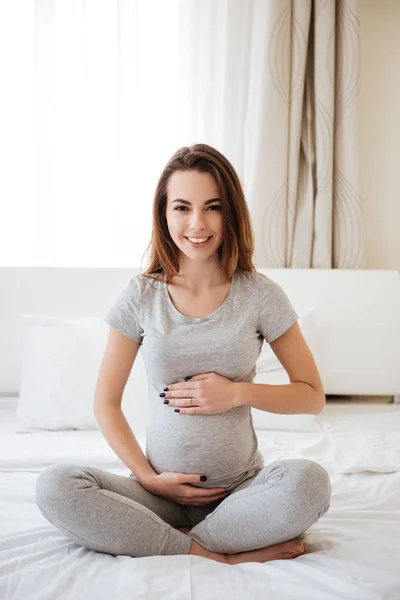 ベッドの上に足を組んで座って陽気な妊娠中の女性 — ストック写真