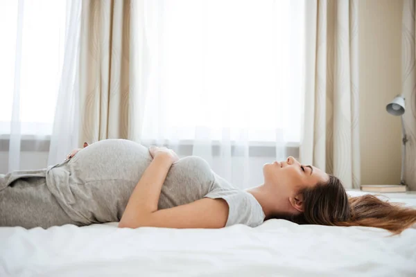Usmívající se těhotná mladá žena lže a relaxaci na lůžku — Stock fotografie