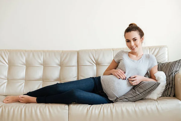 Glada attraktiva gravid ung kvinna ligga och koppla av på soffa — Stockfoto